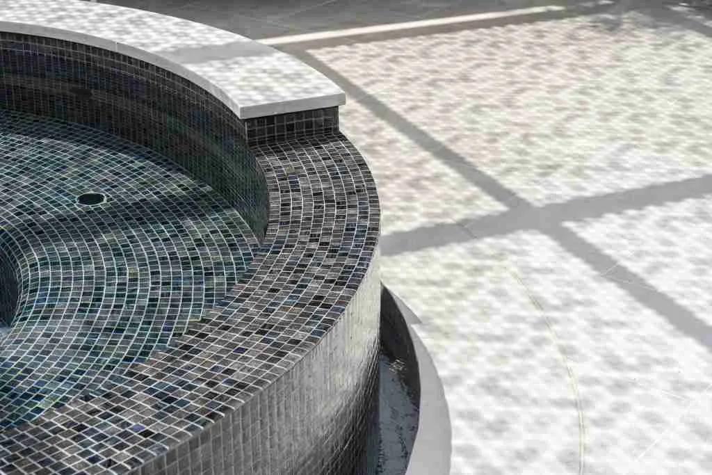 The edge of a rounded Laguna spa with Bisazza black Tripoli tile contrasted against the pool coping